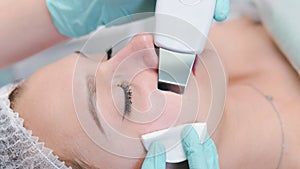 The female cosmetologist makes  a procedure of ultrasonic cleaning face, close-up. Young woman in a beauty salon