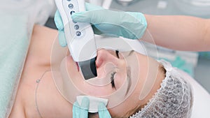 The female cosmetologist makes  a procedure of ultrasonic cleaning face, close-up. Young woman in a beauty salon