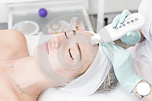 The female cosmetologist makes  a procedure of ultrasonic cleaning face, close-up. Young woman in a beauty salon