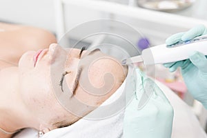 The female cosmetologist makes  a procedure of ultrasonic cleaning face, close-up. Young woman in a beauty salon