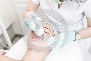 The female cosmetologist makes  a procedure of ultrasonic cleaning face, close-up. Young woman in a beauty salon