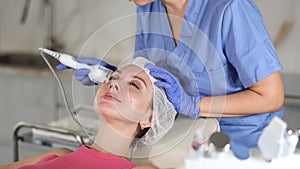 Female cosmetologist performing anti-aging face phototherapy procedure, shrink pores and repair damaged skin for young