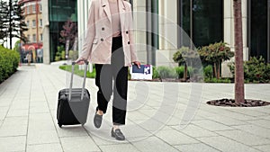 Female in costume and stylish shoes walking on street with luggage in hand