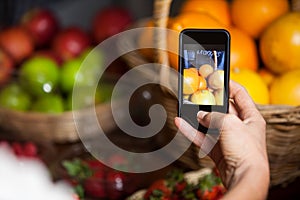 Female costumer taking picture of oranges on mobile phone in organic section