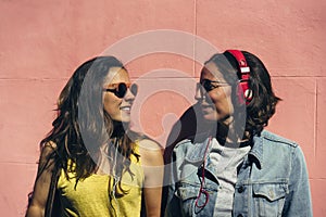 Female couple listening music and spending time together in a pink wall. A pair of young lesbian women couple, concept of same sex