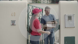 Female courier in red cap delivering package to customers door