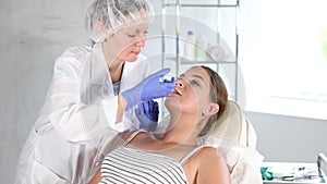 Female cropped doctor in disposable medical mask manipulates correction of size lips to girl patient