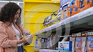 female customer is choosing electric iron in home appliances store