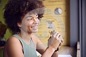 Female Customer In Coffee Shop Window Eating Bagel Sandwich For Lunch