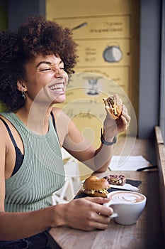 Female Customer In Coffee Shop Window Eating Bagel Sandwich For Lunch