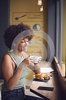 Female Customer In Coffee Shop Window Eating Bagel Sandwich For Lunch