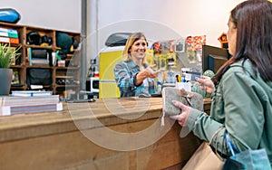 Female customer giving credit card to smiling woman shop assistant to pay purchase on local store