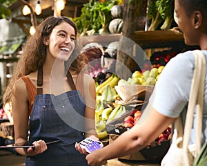 Female Customer At Market Stall Paying For Produce With Contactless Card Payment
