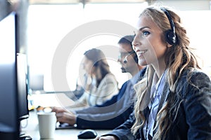 Female customer support operator with headset and smiling, with collegues at background