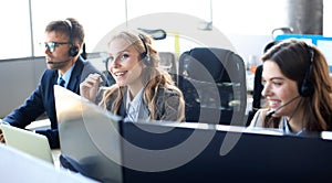 Female customer support operator with headset and smiling, with collegues at background