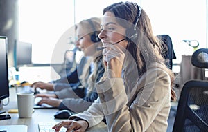 Female customer support operator with headset and smiling, with collegues at background