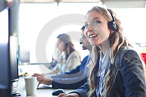 Female customer support operator with headset and smiling, with collegues at background