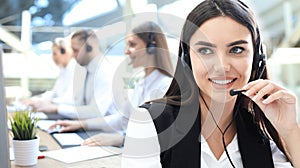 Female customer support operator with headset and smiling, with collegues at background