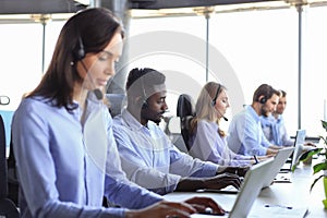 Female customer support operator with headset and smiling, with collegues at background.