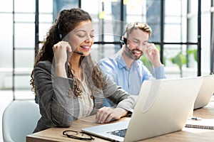 Female customer support operator with headset and smiling, with collegues at background.