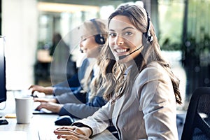 Female customer support operator with headset and smiling, with collegues at background