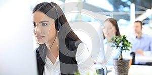 Female customer support operator with headset and smiling, with collegues at background photo