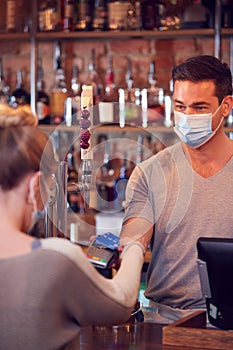 Female Customer Wearing Mask In Bar Making Contactless Payment For Drinks During Health Pandemic