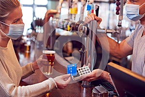 Female Customer Wearing Mask In Bar Making Contactless Payment For Drinks During Health Pandemic