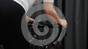 Female cycling indoors out of saddle hard pedaling on smart trainer. Hands holding handlebar with cycling computer showing speed a