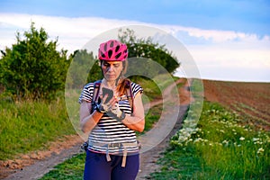 Female cyclist checking her phone for directions on an MTB route in the countryside, at sunset.
