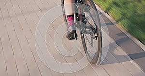 Female cyclist is speeding on road bike in sunshine. Bicycle wheel in motion. Woman is riding road bicycle in park. Bike wheel rot