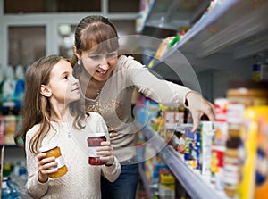 Female with daughter choosing canned goods in food store