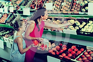 Female with daughter selecting apples in fruit section