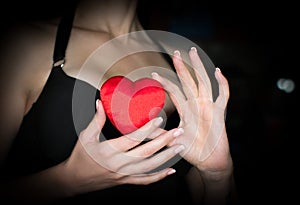 Female decolletage, black dress. Woman holds a red silk heart in her hands, low key.