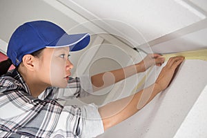 female decorator applying masking tape along join wall and ceiling