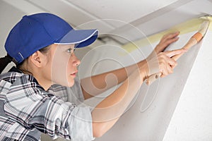 female decorator pressing masking tape to ceiling with brush