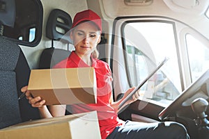 Female delivery service worker in red uniform sitting in van and working with packages