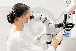 Female dentist advanced user, dental tools. Looking into the lens of a microscope while examining his patients teeth. in