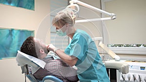 Female dentist checks up teeth of male patient.