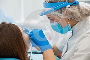 Female dentist curing teeth cavity in blue gloves and protective mask.