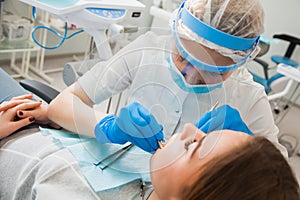 Female dentist curing teeth cavity in blue gloves and protective mask.