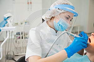 Female dentist curing teeth cavity in blue gloves and protective mask.