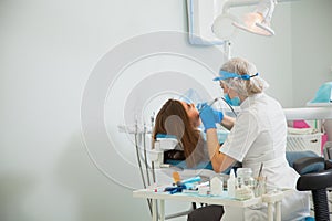 Female dentist curing teeth cavity in blue gloves and protective mask.