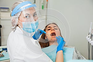 Female dentist curing teeth cavity in blue gloves and protective mask.