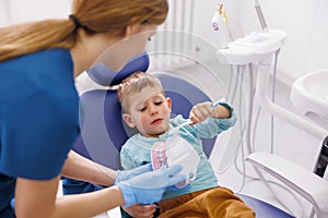 Female dentist demonstrating proper tooth brushing technique to child patient