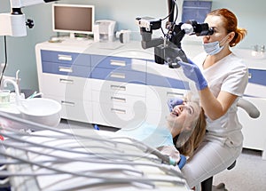 Female dentist with dental tools - microscope, mirror and probe treating patient. Medicine, dentistry and health care