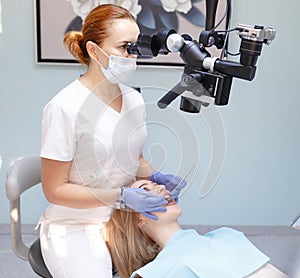 Female dentist with dental tools - microscope, mirror and probe treating patient. Medicine, dentistry and health care
