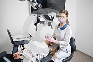 Female dentist with dental tools - microscope, mirror and probe treating patient teeth at dental clinic office