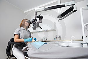 Female dentist with dental tools and microscope treating patient teeth at dental clinic office. Medicine, dentistry and