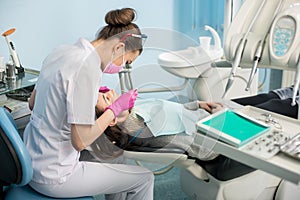 Female dentist with dental tools - mirror and probe checking up patient teeth at dental clinic office